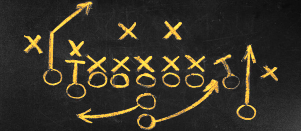 Football play in Xs and Os drawn in orange chalk on a black board.